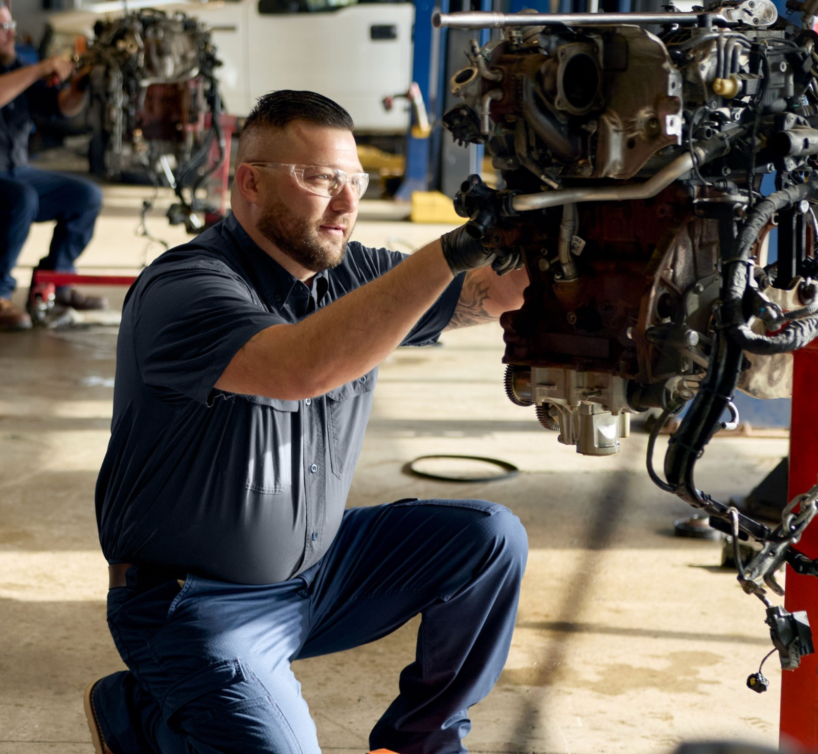 Mechanic in a navy work shirt repairing an engine in a service shop
